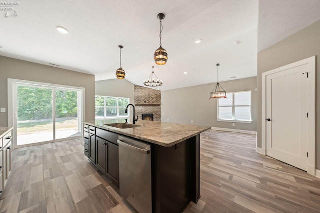 kitchen with a fireplace, light wood finished floors, stainless steel dishwasher, vaulted ceiling, and a sink