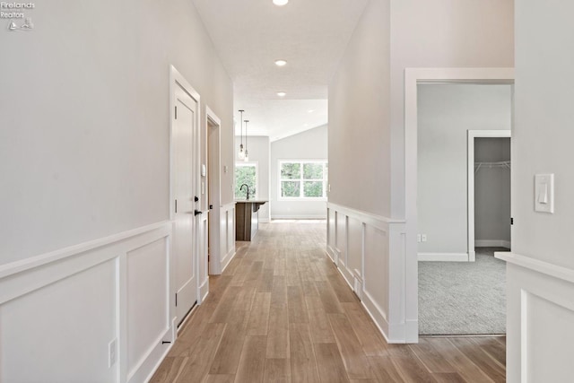 hall featuring light wood-type flooring, a wainscoted wall, a decorative wall, and recessed lighting