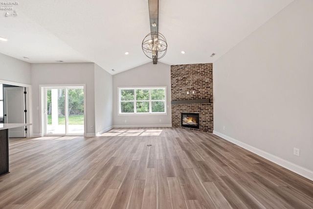 unfurnished living room featuring baseboards, light wood-style flooring, vaulted ceiling with beams, an inviting chandelier, and a brick fireplace