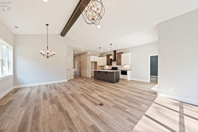 unfurnished living room featuring beam ceiling, light wood finished floors, a sink, a chandelier, and baseboards