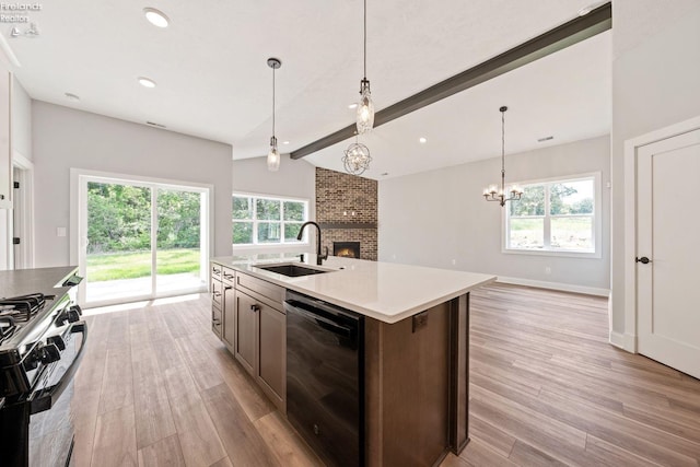 kitchen with black dishwasher, light wood finished floors, a brick fireplace, a sink, and gas range