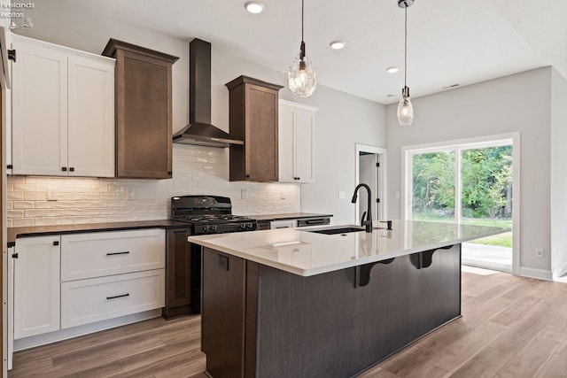 kitchen with backsplash, black range with gas cooktop, a sink, wall chimney range hood, and light wood-type flooring