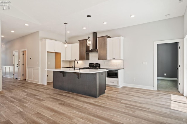 kitchen featuring wall chimney exhaust hood, stove, backsplash, and light wood-style floors