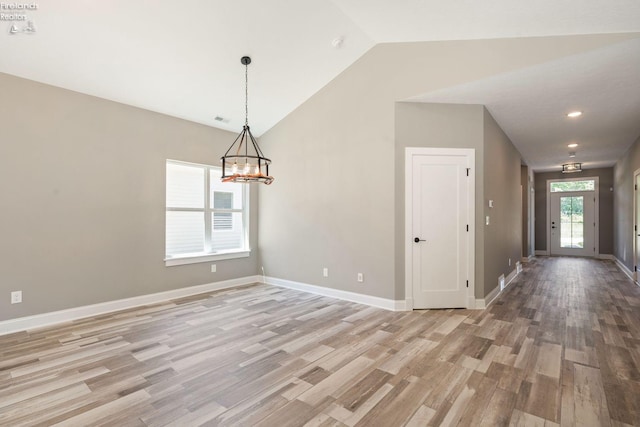 spare room featuring light wood finished floors, visible vents, baseboards, lofted ceiling, and a chandelier