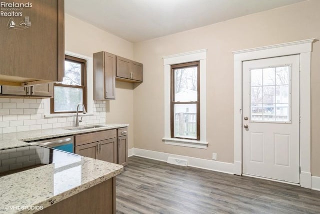 kitchen with dark hardwood / wood-style flooring, tasteful backsplash, light stone counters, and sink