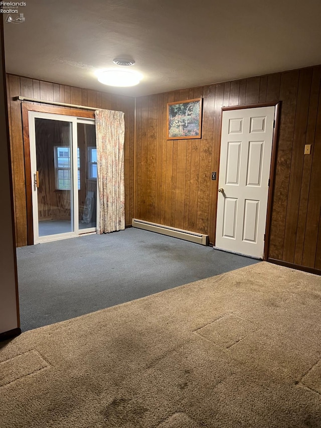 spare room featuring carpet floors, baseboard heating, and wooden walls