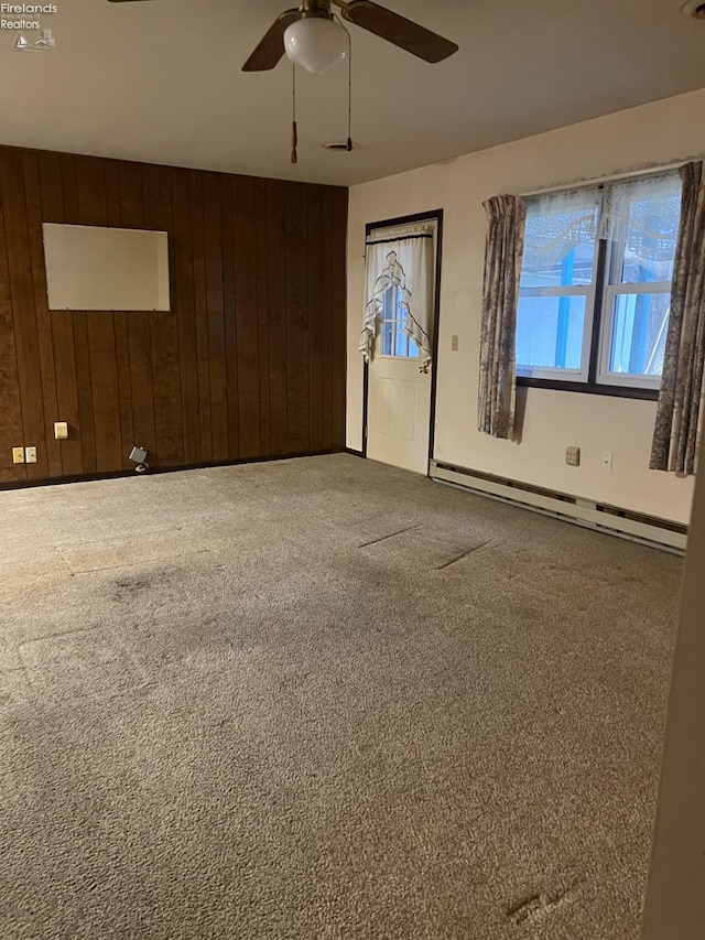 unfurnished room featuring carpet flooring, wood walls, ceiling fan, and a baseboard radiator