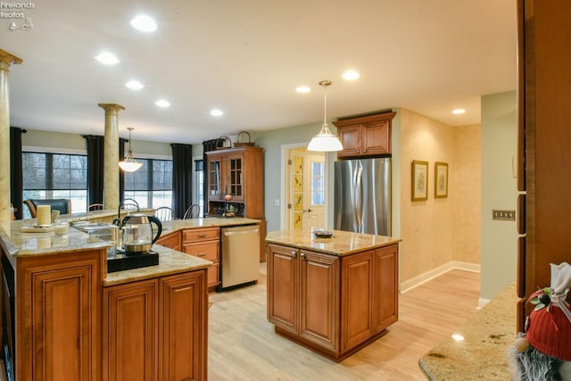 kitchen with light stone countertops, light hardwood / wood-style flooring, decorative light fixtures, a kitchen island with sink, and appliances with stainless steel finishes