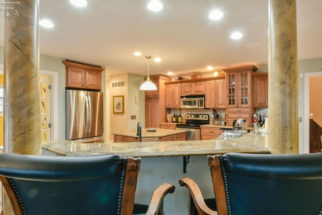 kitchen with a breakfast bar, appliances with stainless steel finishes, decorative light fixtures, light stone counters, and kitchen peninsula