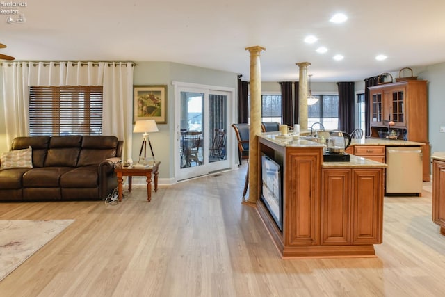 kitchen with decorative columns, pendant lighting, light hardwood / wood-style flooring, dishwasher, and an island with sink