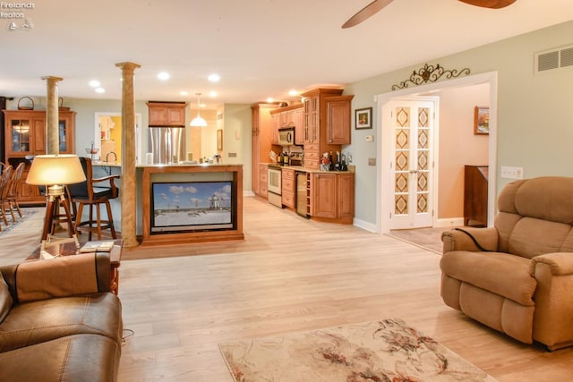 living room featuring light wood-type flooring, ornate columns, ceiling fan, and beverage cooler