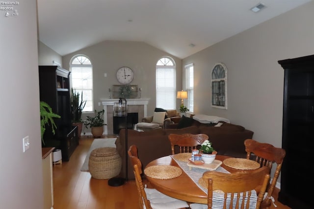 dining space with light hardwood / wood-style floors, lofted ceiling, and a tile fireplace