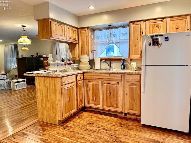 kitchen featuring white fridge, pendant lighting, kitchen peninsula, sink, and light hardwood / wood-style flooring