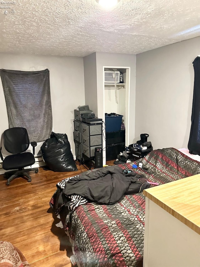 bedroom with a wall mounted air conditioner, hardwood / wood-style floors, and a textured ceiling