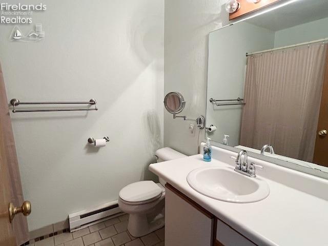 bathroom with curtained shower, baseboard heating, tile patterned flooring, toilet, and vanity