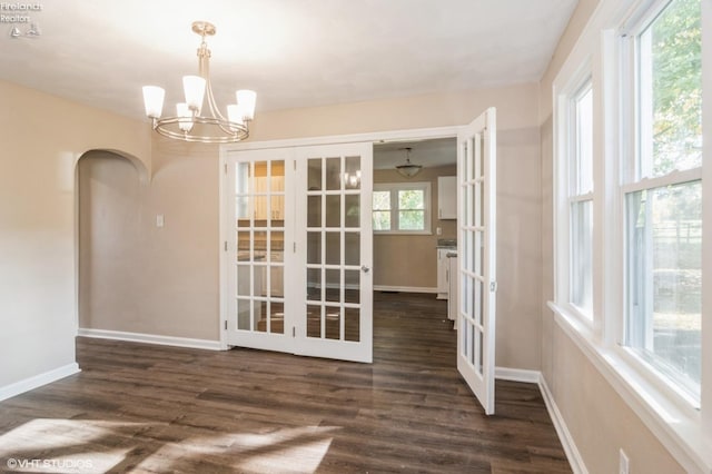 unfurnished dining area with french doors, dark wood-type flooring, and a notable chandelier