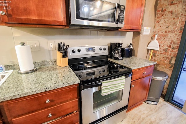 kitchen with light stone countertops, stainless steel appliances, and brick wall