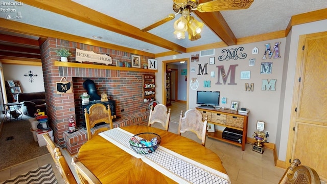 tiled dining space with beam ceiling, a textured ceiling, a wood stove, and ceiling fan