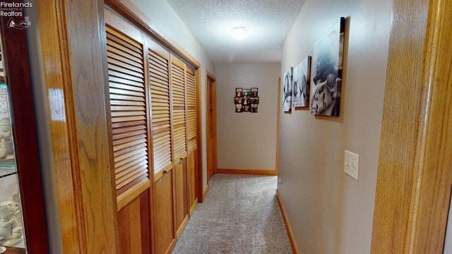 hall with a textured ceiling and light colored carpet