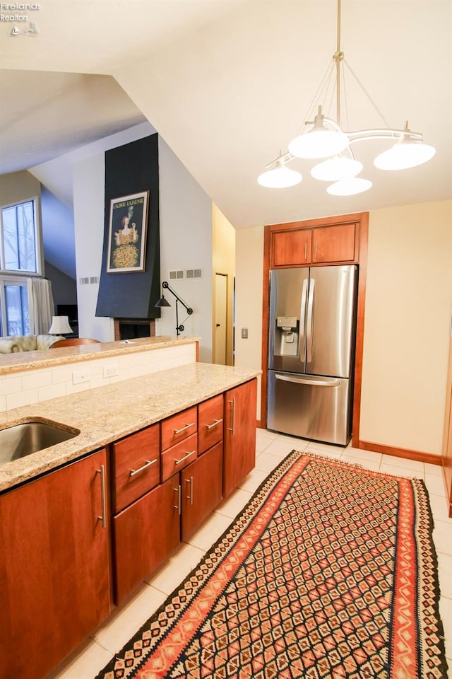 kitchen featuring light stone countertops, stainless steel refrigerator with ice dispenser, sink, light tile patterned floors, and hanging light fixtures