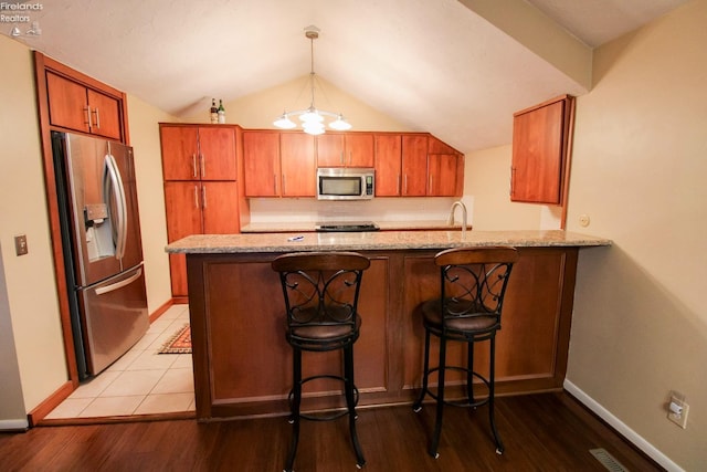 kitchen featuring a breakfast bar, light wood-type flooring, decorative light fixtures, kitchen peninsula, and stainless steel appliances