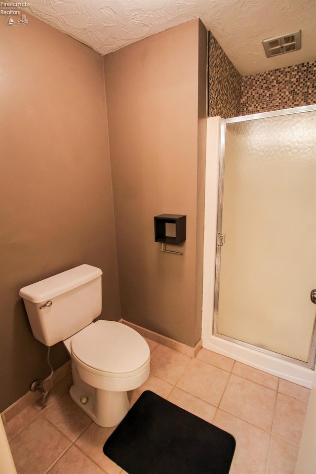 bathroom with toilet, a textured ceiling, tile patterned floors, and a shower with door