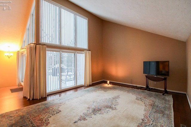 unfurnished living room with hardwood / wood-style flooring, a notable chandelier, a healthy amount of sunlight, and high vaulted ceiling