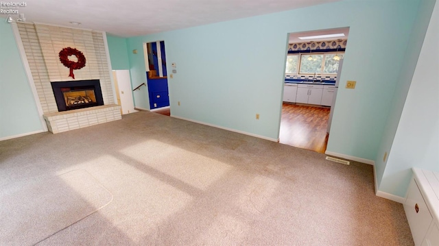 unfurnished living room featuring sink, carpet flooring, and a fireplace