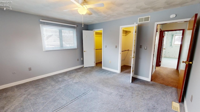 unfurnished bedroom with ceiling fan, a closet, a walk in closet, and carpet flooring