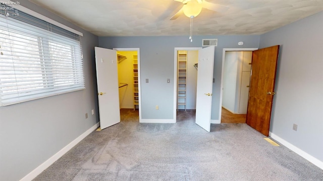 unfurnished bedroom featuring ceiling fan, carpet, a closet, and a walk in closet