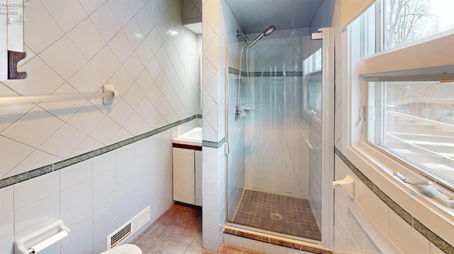 bathroom with a shower with door, tile walls, tile patterned floors, and a healthy amount of sunlight