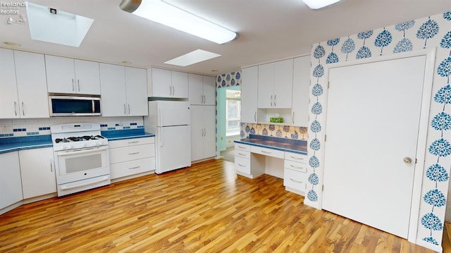 kitchen featuring white appliances, white cabinets, a skylight, tasteful backsplash, and light hardwood / wood-style floors