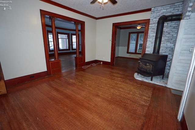 unfurnished living room with a wood stove, ceiling fan, dark wood-type flooring, crown molding, and a textured ceiling