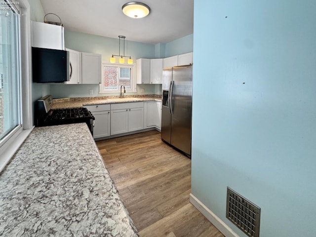 kitchen featuring white cabinetry, stainless steel refrigerator with ice dispenser, hanging light fixtures, black stove, and sink