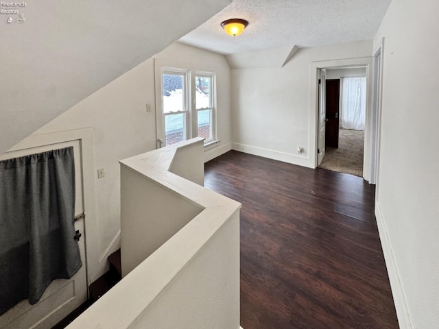 interior space with a textured ceiling, dark wood-type flooring, and lofted ceiling