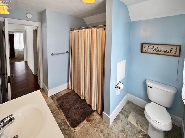 bathroom featuring toilet, sink, a textured ceiling, vaulted ceiling, and curtained shower