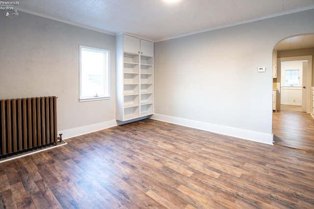 empty room featuring dark wood-type flooring, ornamental molding, radiator heating unit, and built in features