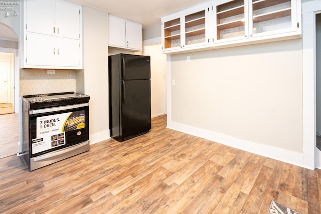 kitchen with tasteful backsplash, white cabinetry, black fridge, and light hardwood / wood-style flooring