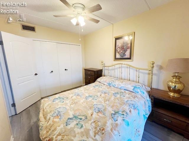 bedroom with wood-type flooring, a textured ceiling, ceiling fan, and a closet