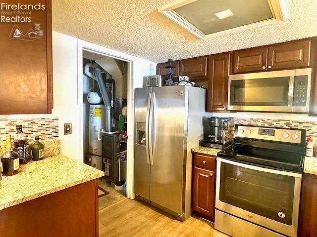 kitchen featuring stainless steel appliances, light stone countertops, decorative backsplash, light hardwood / wood-style flooring, and gas water heater