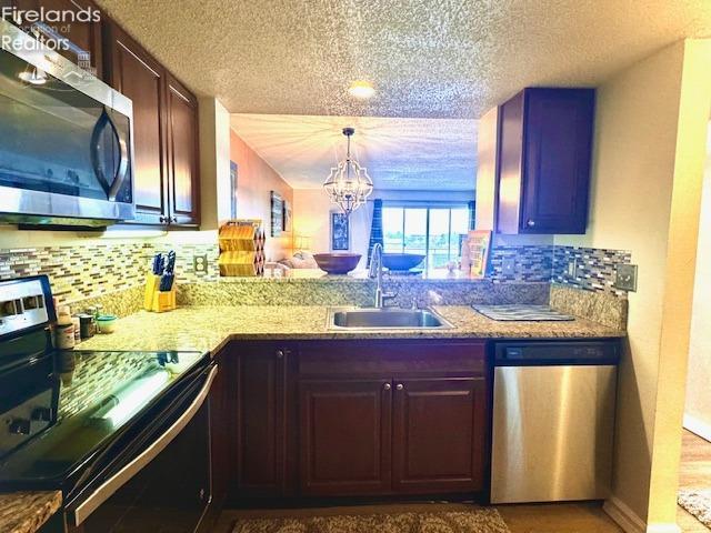 kitchen with an inviting chandelier, appliances with stainless steel finishes, tasteful backsplash, and sink