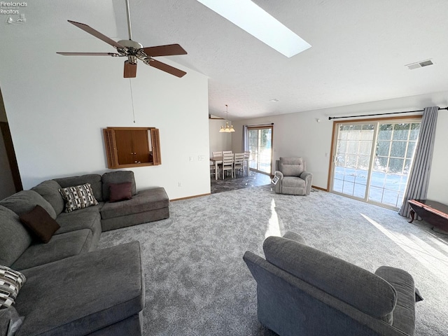 living room featuring ceiling fan with notable chandelier, high vaulted ceiling, a skylight, and dark colored carpet