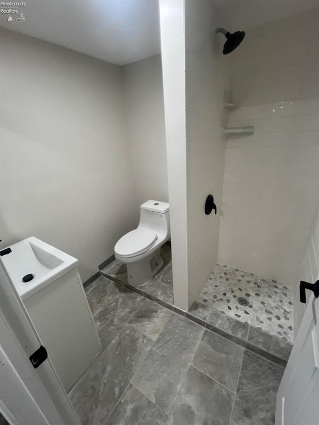 bathroom with toilet, vanity, and tiled shower