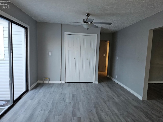 unfurnished bedroom with a textured ceiling, multiple windows, hardwood / wood-style flooring, a closet, and ceiling fan