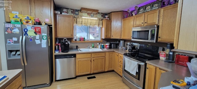 kitchen featuring a textured ceiling, appliances with stainless steel finishes, light wood-type flooring, and sink