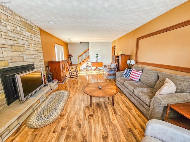 living room featuring a stone fireplace, a textured ceiling, and hardwood / wood-style flooring