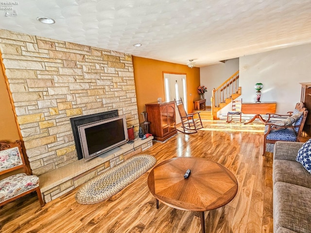 living room with a textured ceiling, hardwood / wood-style floors, and a stone fireplace