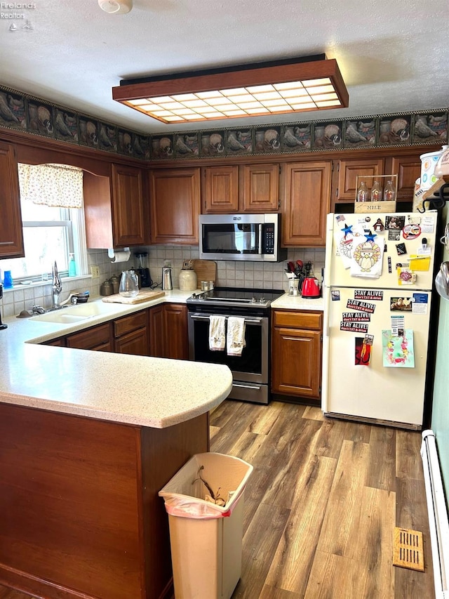 kitchen with wood-type flooring, kitchen peninsula, stainless steel appliances, and a baseboard radiator