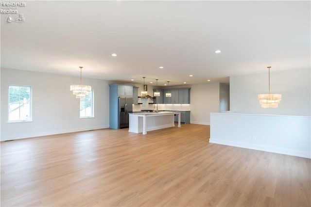 unfurnished living room with an inviting chandelier, light hardwood / wood-style flooring, and sink