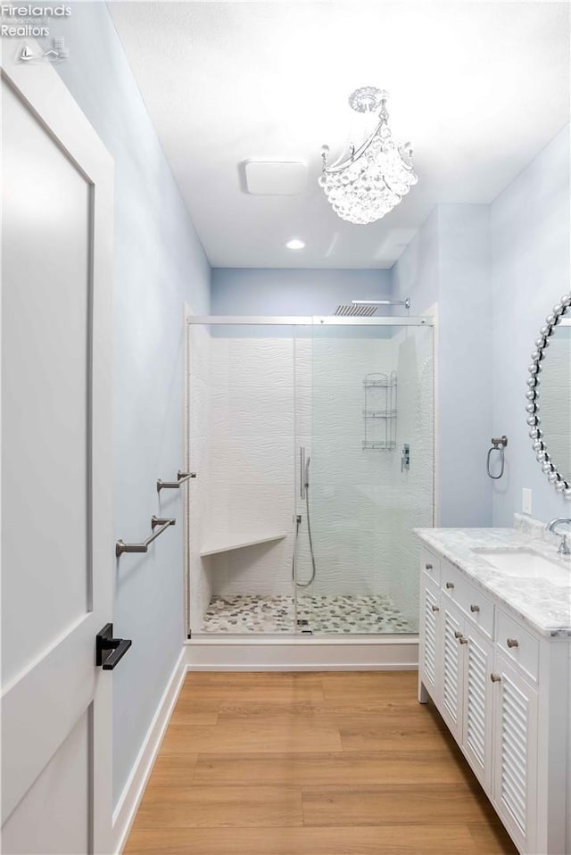 bathroom with vanity, a shower with door, an inviting chandelier, and hardwood / wood-style floors